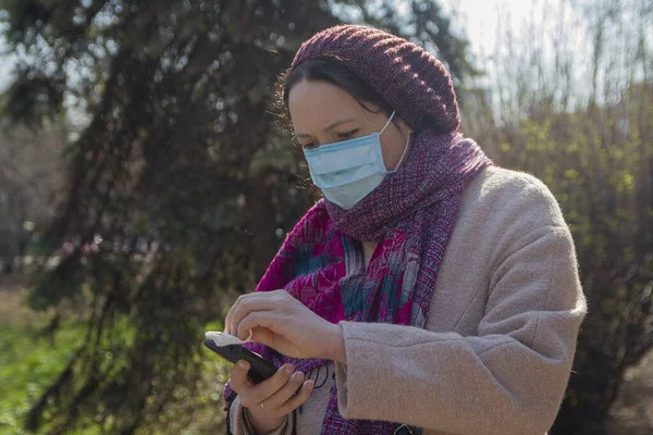 Serious woman in a protective mask with a smartphone. People