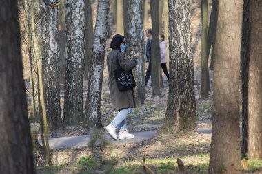 Kiev, Ukrayna - 19 Mart 2020: Karantina döneminde parkta yürüyüş yapan koruyucu tıbbi maskeli insanlar