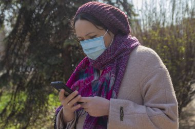 Akıllı telefonlu koruyucu maskeli ciddi bir kadın. İnsanlar
