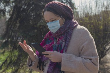 Akıllı telefonlu koruyucu maskeli ciddi bir kadın. İnsanlar