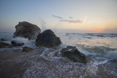 Gün batımında dalgalar plajda kayalara vuruyor. Kırım