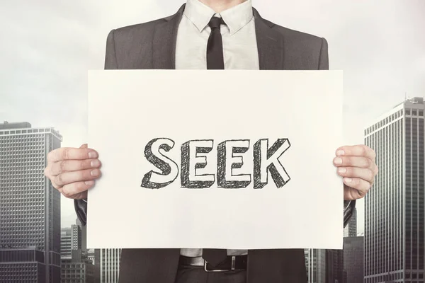 Businessman Holding Placard With Seek Text Against Buildings — Stock Photo, Image