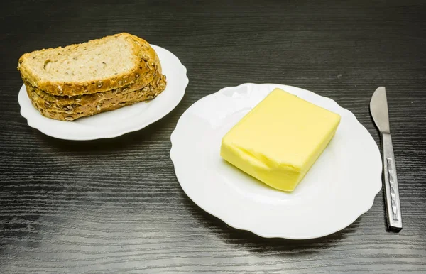 Manteiga e pão em pratos brancos e uma faca na mesa . — Fotografia de Stock