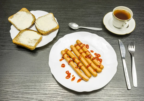 Desayuno: salchichas hervidas con ketchup, rebanadas con mantequilla y una taza de té . —  Fotos de Stock
