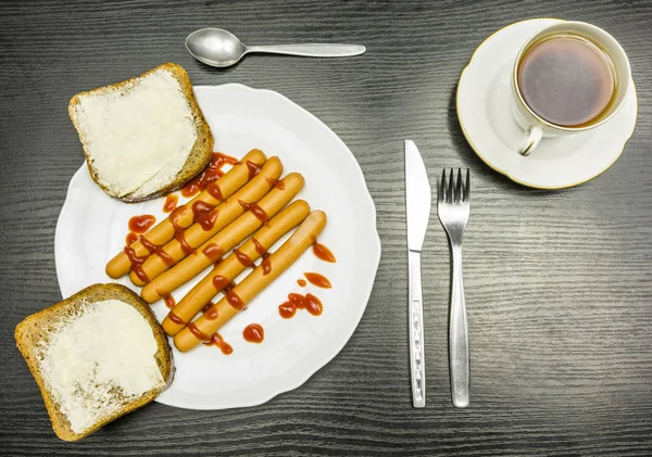 Un plato de salchichas hervidas con ketchup y una taza de té caliente. Vista desde arriba . — Foto de Stock