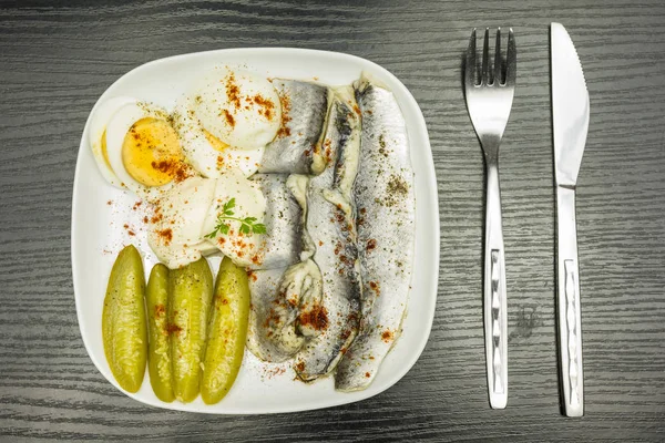 Placa branca com arenque marinado em óleo, ovo cozido fervido, pepino e maionese. Temperado com pimenta preta e páprica vermelha. Vista de cima . — Fotografia de Stock