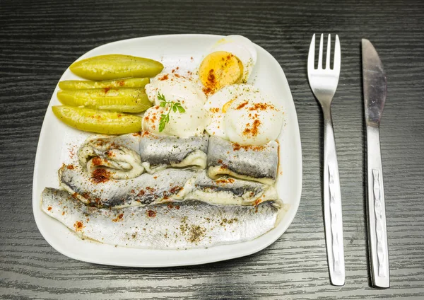 Placa branca com arenque marinado em óleo, ovo cozido fervido, pepino e maionese. Temperado com pimenta e páprica . — Fotografia de Stock