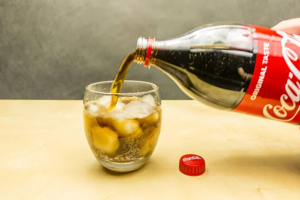 Coca-Cola aus der Flasche in ein Glas mit Eiswürfeln gießen. — Stockfoto