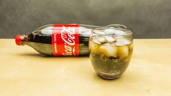 Ein Glas Coca Cola mit Eiswürfeln. Flasche im Hintergrund. — Stockfoto