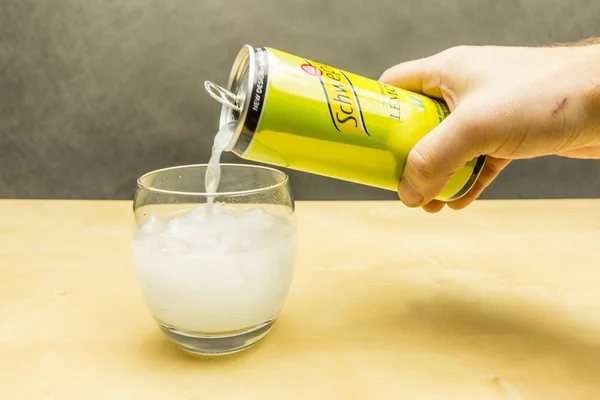 将碳酸饮料从柠檬味的 schweppes 倒入冰块中的玻璃杯中。. — 图库照片