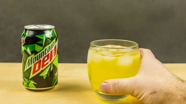 A glass of Mountain Dew with ice cubes held in hand. — Stock Photo, Image