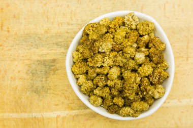 Beyaz dut bir ahşap tahta üzerinde bir kasede kurutulmuş meyve. Yukarıdan görüntülemek.