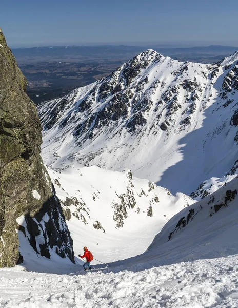 A skier in a red jacket during a downhill ride in a couloir in the mountains. — Stock Photo, Image