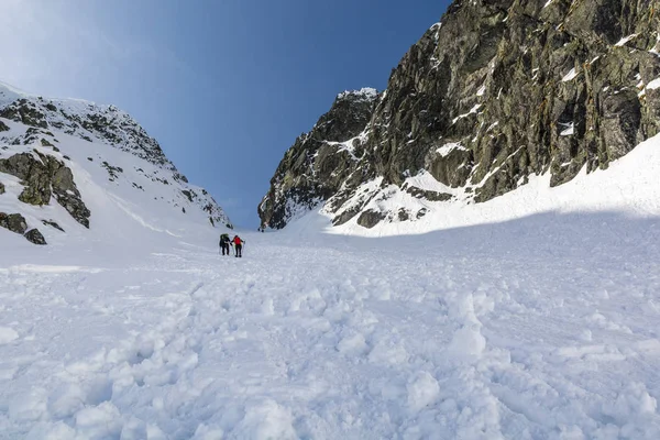 Tourists come up with a snow-capped couloir to the mountain pass. — Stock Photo, Image