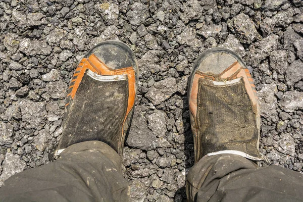 Muddy mountaineering boots after a mountain trip presented on crushed asphalt.