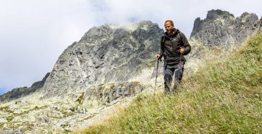 Stary Smokovec, Slovakya - 12 Eylül 2019: Dağlarda ve yürüyüş direkleri ile rüzgarlı bir günde yumuşak kabuklu bir ceket giyen yürüyüşçü.