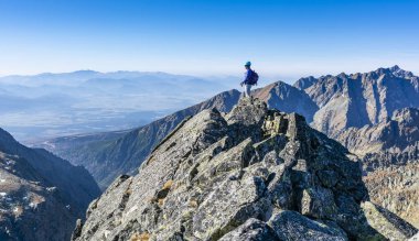 Strbske Pleso, Slovakya - 25 Ekim 2019: Kasklı ve güneş gözlüklü bir kadın dağın zirvesinden hayranlık duyuyor, etrafındaki dağ ve vadilerin muhteşem manzarası.