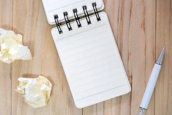 Kleines Notizbuchpapier (Notizblock) zum Schreiben von Informationen mit Stift und zerknüllten Papierkugeln auf einem Holztisch. Blick von oben — Stockfoto