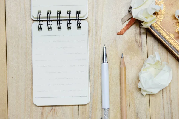 Kleines Notizbuchpapier (Notizblock) zum Schreiben von Informationen mit Stift, Bleistift, Buch und zerknüllten Papierkugeln auf einem Holztisch. Blick von oben — Stockfoto