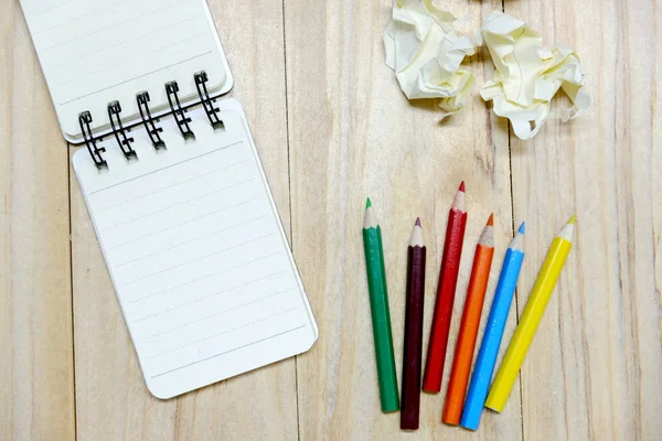 Papel de libreta pequeña (bloc de notas) para escribir información con lápiz de color y bolas de papel arrugado en la mesa de madera. vista desde arriba — Foto de Stock