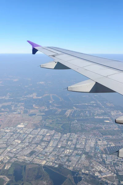 Ala del avión volando sobre la ciudad. Vista desde la ventana de un avión — Foto de Stock