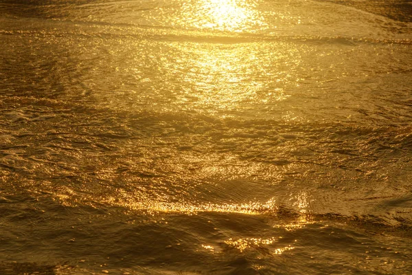 Cahaya emas memantulkan gelombang air di laut dan pasir saat matahari terbenam. Tone Emas Murni — Stok Foto