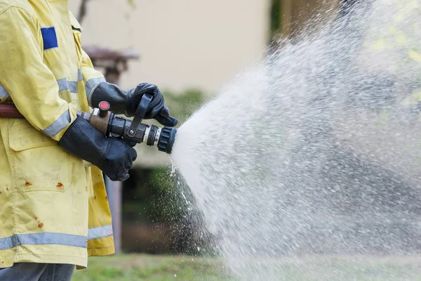 Firefighter holding high pressure fire hose nozzle. Firefighters training. - Water jet splashing