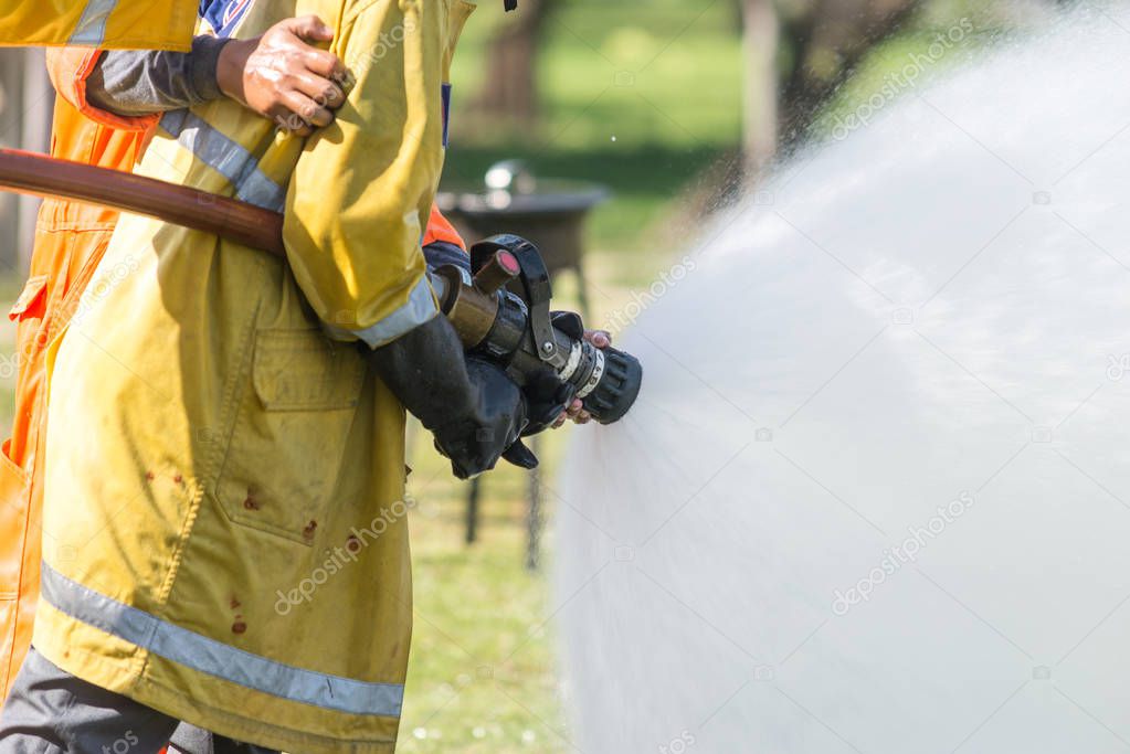 Firefighter holding high pressure fire hose nozzle. Firefighters training. - Water jet splashing