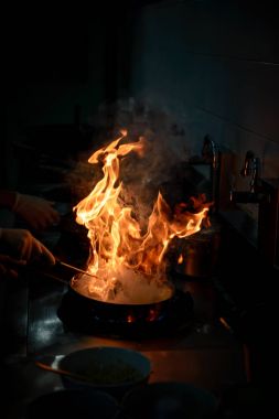 Aşçı lokanta mutfağında yemek pişiriyor ve ateş yakıyor.