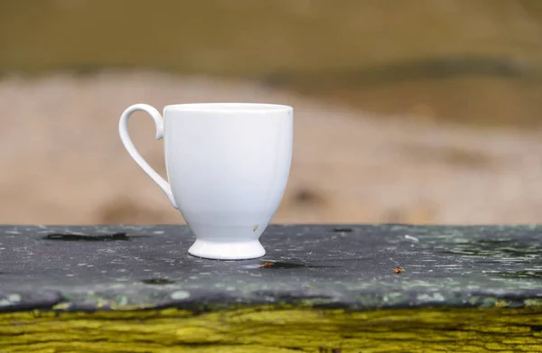 Белая чашка горячего кофе на деревянном столе в открытом природном кафе — стоковое фото