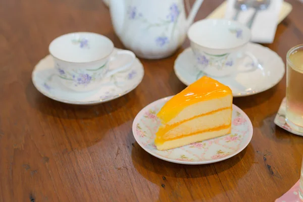 Piece of delicious orange cake with teapot and cup of tea on wooden table — Stock Photo, Image