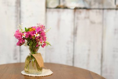 Cam vazodaki güzel çiçekler ahşap masada duruyor. Klasik tarzda ev dekorasyonu