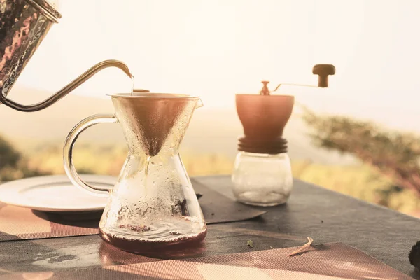 Hand drip coffee making pour over coffee with hot water being poured from a kettle with mountain view and natural green view feeling chill and relax in nature
