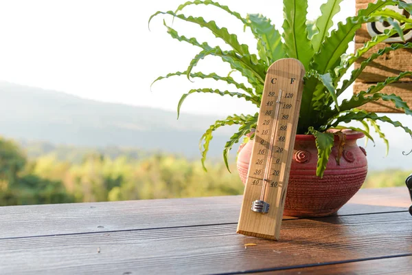 Outdoor wood thermometer calibrated in celsius and fahrenheit scale showing 15 degrees celsius or 60 degrees fahrenheit on terrace with landscape mountains view