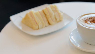 Sabahları kahvaltıda bir fincan sıcak kapuçino ve sandviç.