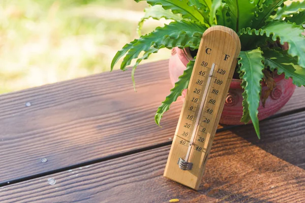 Outdoor wood thermometer calibrated in celsius and fahrenheit scale showing 15 degrees celsius or 60 degrees fahrenheit on terrace with landscape mountains view