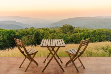 Boş ahşap masa ve terasta sandalyeler. Gün batımında manzara dağları manzaralı güzel koltuklar..