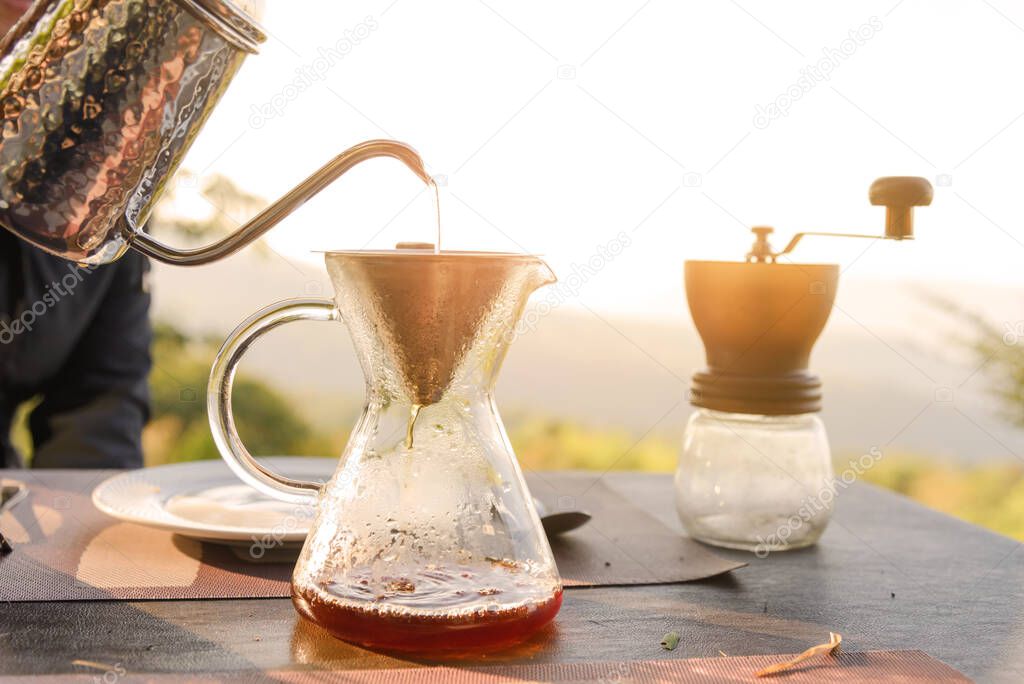 Hand drip coffee making pour over coffee with hot water being poured from a kettle with mountain view and natural green view feeling chill and relax in nature