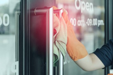 Kadın elinde yeşil mikrofiber eldiven tutan, sterilize edici sprey kullanan ve toz silen koruyucu turuncu lastik eldivenlerle temizlik ve dezenfeksiyon yapar.