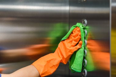Kadın elinde yeşil mikrofiber eldiven tutan, sterilize edici sprey kullanan ve toz silen koruyucu turuncu lastik eldivenlerle temizlik ve dezenfeksiyon yapar.