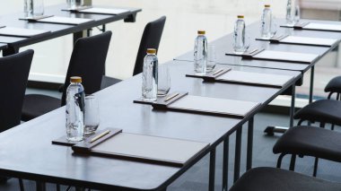Plastik su şişeleri, kalem ve beyaz kağıtlı içki bardakları otel konferans odasında seminer ya da iş toplantısı için hazırlandı.