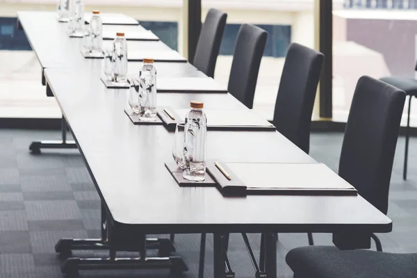 Plastic water bottles, Drinking glasses with pencil and white papers setup on the table prepared for seminar or business meeting in the hotel conference room