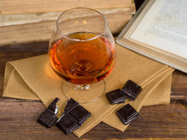 Bardak brendi ve kitaplar ile ahşap masa çikolata