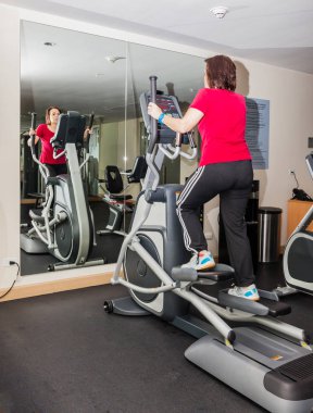 Kadın bir crosstrainer büyük bir ayna önünde üzerinde eğitim.