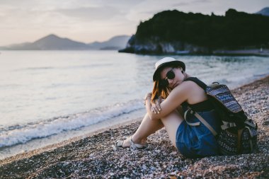 Gün batımında çakıl plajı deniz kenarında oturan kadın