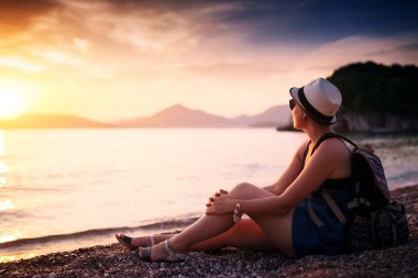 Gün batımında çakıl plajı deniz kenarında oturan kadın