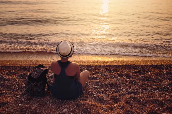 Gün batımında çakıl kenarı deniz kenarında oturan kadın