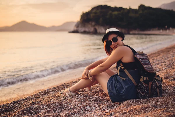 Gün batımında çakıl plajı deniz kenarında oturan kadın