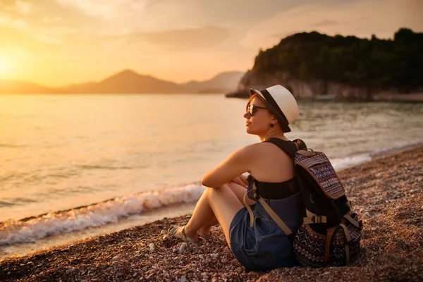 Gün batımında çakıl plajı deniz kenarında oturan kadın