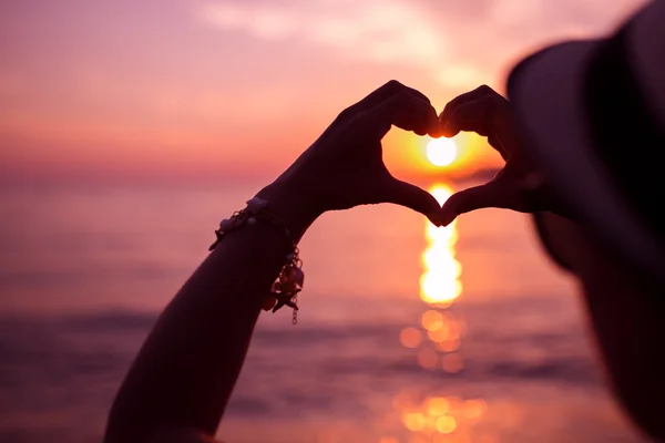 Vrouw maken van hart voor handen in de buurt van de zee bij zonsondergang — Stockfoto